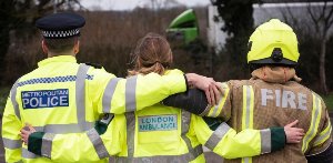 Police officer, paramedic, and firefighter standing together with arms around each other.