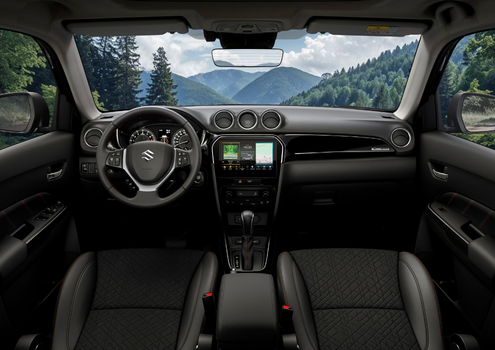 Car interior with black seats and a touchscreen on the dashboard, overlooking a mountain view.